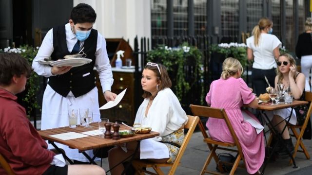 Man in mask serves diners outdoors