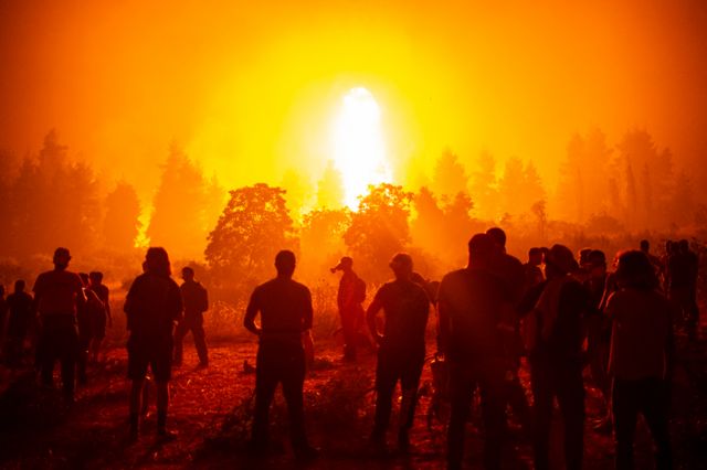 Local volunteers gather in an open field and wait to support fire fighters during a wildfire next to the village of Kamatriades, Evia island, Greece